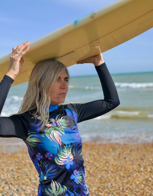 Model posing with surfboard in a long-sleeve black and blue floral rash vest